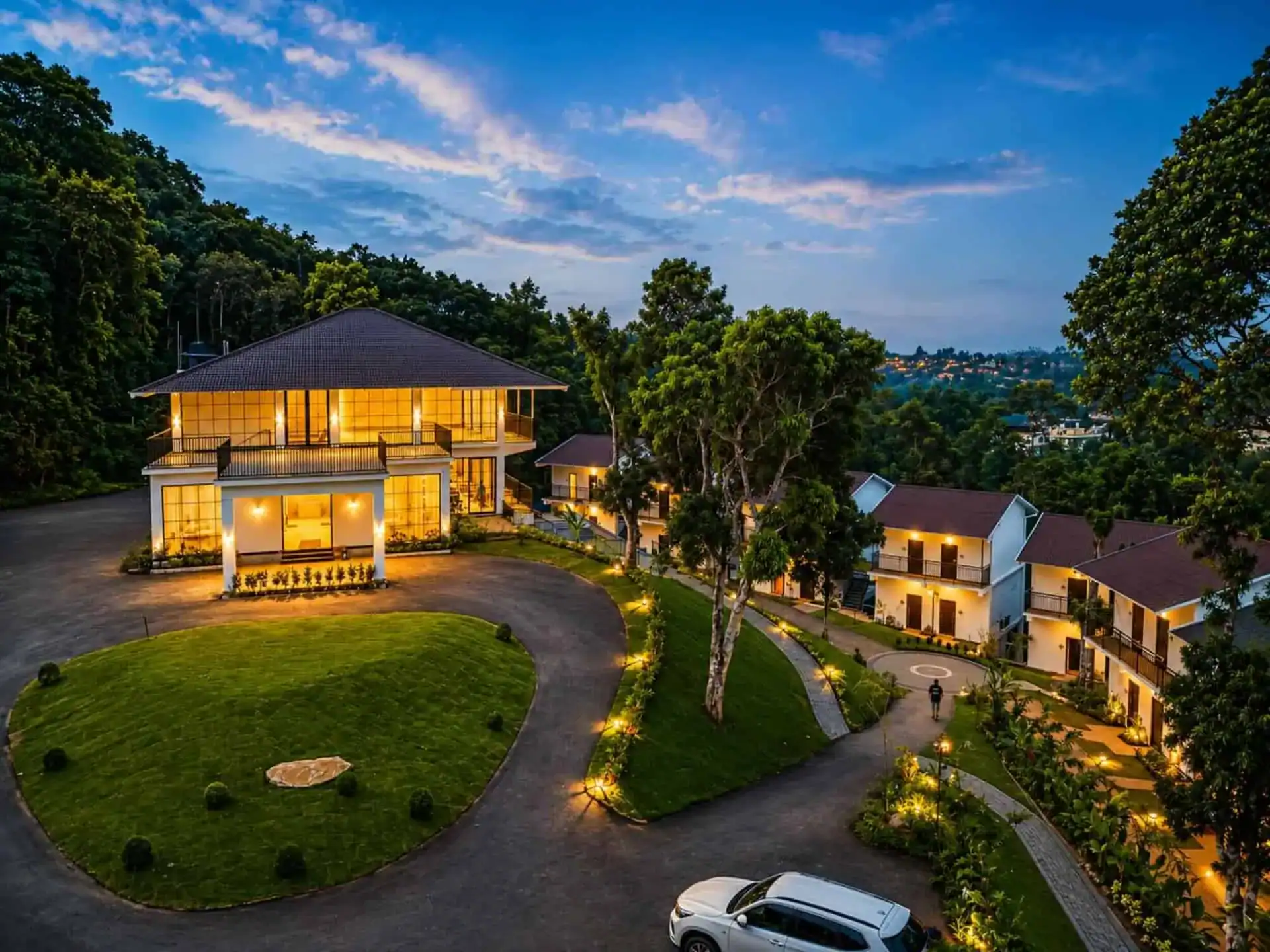 Vega Munnar Resort main building and cottage block at blue-hour dusk with warm amber lighting and circular driveway