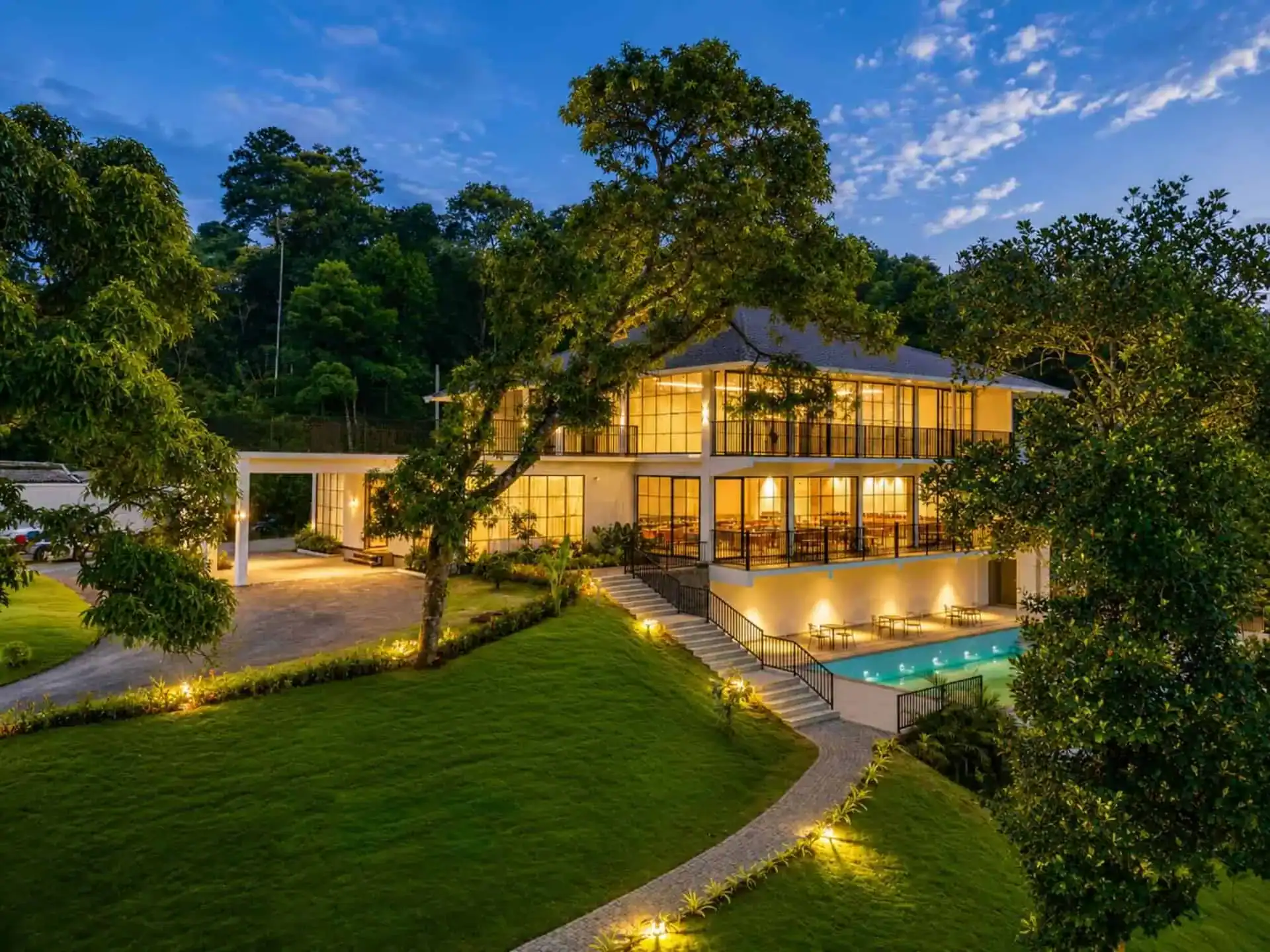 Vega Munnar Resort main building glowing at dusk with winding garden path and turquoise pool