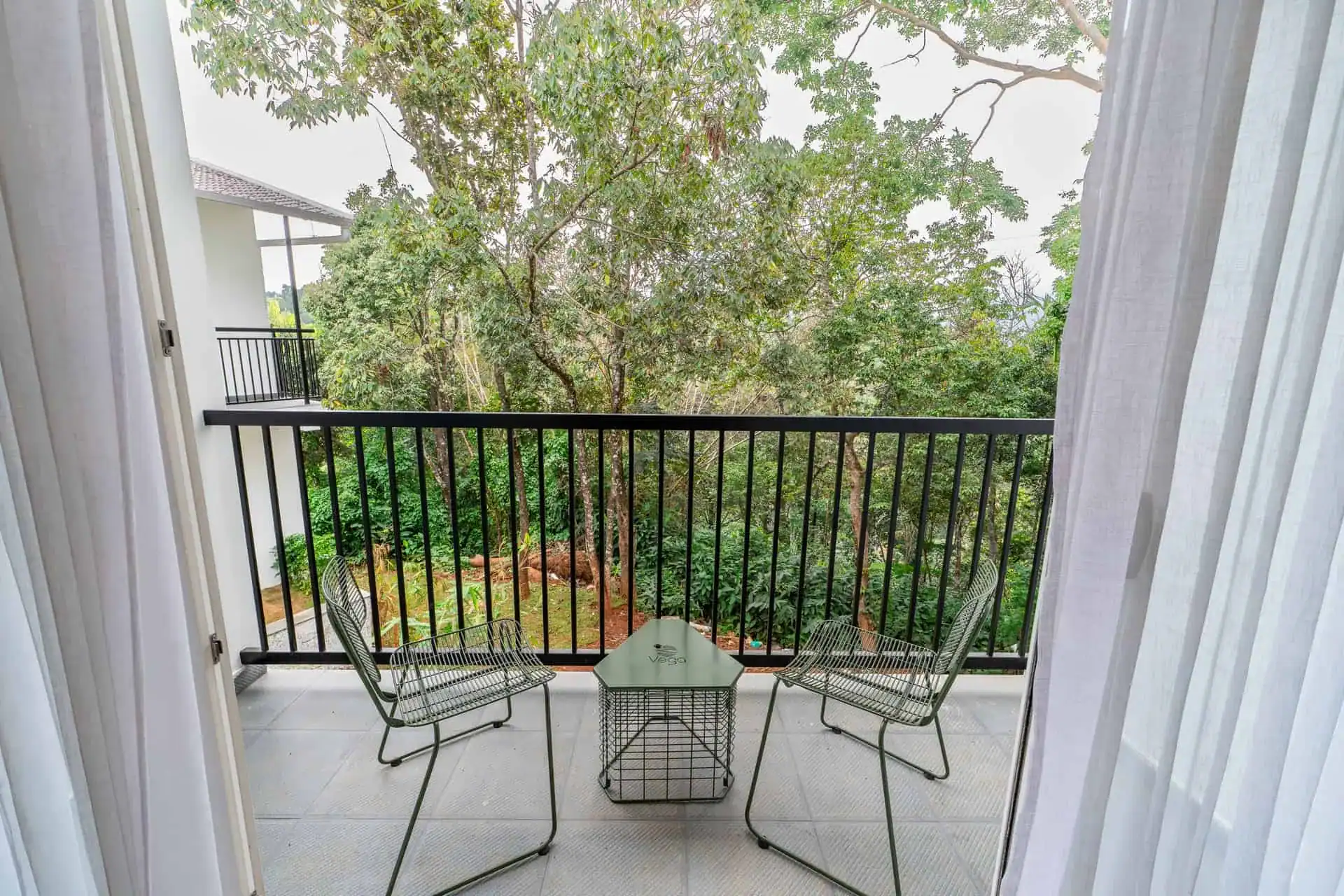 View through parted curtains onto private balcony with wire chairs and tropical canopy
